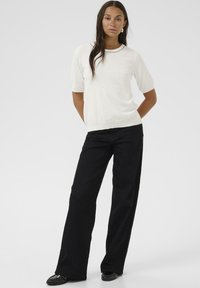 Haut en tricot blanc à manches courtes avec un col rond, associé à un pantalon large noir. La tenue présente une texture lisse et des lignes épurées.