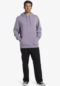 Felpa viola chiaro con cappuccio e lacci, tasca anteriore a marsupio, orlo e polsini a coste, abbinata a pantaloni neri e sneakers nere.