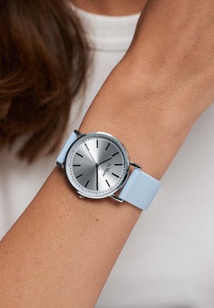 Silberne Armbanduhr mit rundem Zifferblatt, blauem Silikonarmband und minimalistischen Stundenmarkierungen. Sie verfügt über eine glatte metallische Oberfläche und ein dezentes Logo.