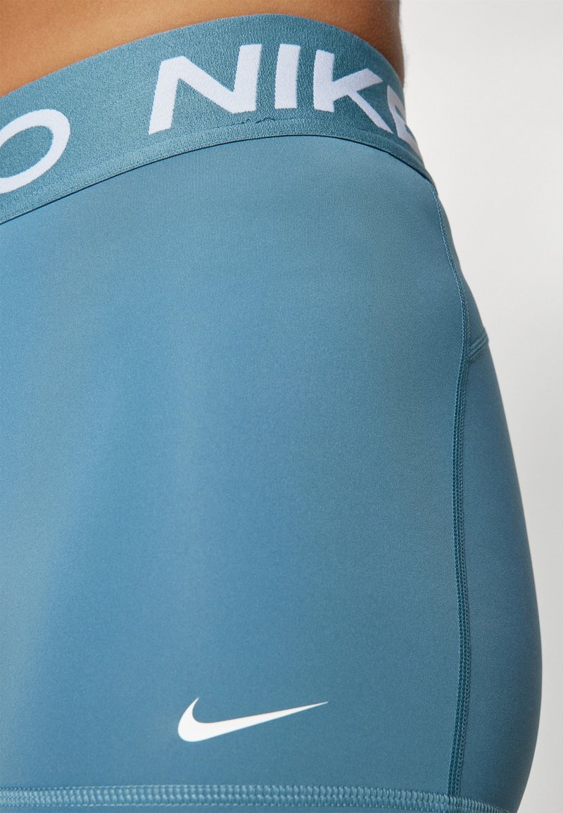 Pantaloni corti sportivi blu con un logo Nike bianco sulla cintura. Realizzati in un materiale liscio e elasticizzato, con un design aderente e cuciture piatte.