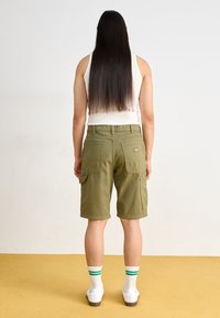 Green cargo shorts with side pockets, positioned above the knee. Paired with white ankle socks featuring green stripes and white sneakers.