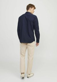 Marineblå skjorte med knapper, lige pasform, lavet af bomuldsstof, lange ærmer og buet kant, parret med lysebeige bukser og sneakers.