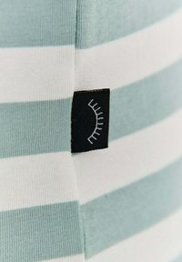 Páskovaná látka s alternujícími světle modrými a bílými barvami. Černý štítek s bílým lineárním ztvárněním řas. Hladká textura.