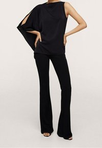Haut sans manches noir avec un design asymétrique et des accents découpés, associé à un pantalon noir évasé. Tissu lisse avec une texture douce.