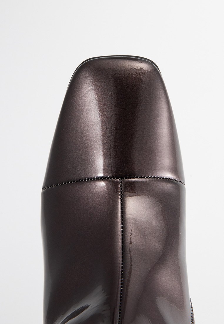 Stivali ankle in pelle verniciata marrone con punta quadrata, texture liscia e cuciture precise lungo le cuciture.