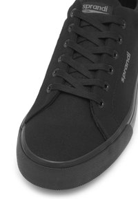 Zapatilla baja negra con suela de goma texturizada, parte superior de tela, cordones negros y logo "sprandi" en la lengüeta y el costado.