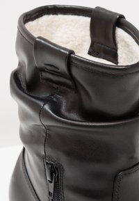 Bottines en cuir noir avec une doublure intérieure douce blanche, design semi-flottant et détail de fermeture à glissière sur le côté.