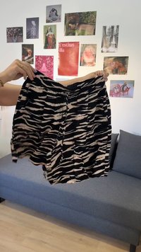 Mains tenant un short noir et blanc à motif zèbre devant un mur blanc avec diverses images colorées et un canapé gris en dessous.