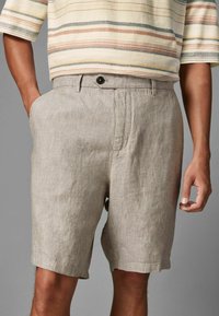 Ljusbeige linshorts med fickor, med en mjuk textur och en knappstängning i midjan. Skräddarsydd, knälång design.