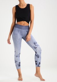 Zwarte korte tanktop met geknoopte voorkant en blauwe tie-dye legging met gestructureerde patronen en een hoge tailleband.