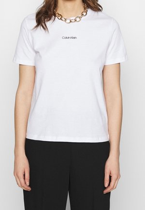 Hvid bomulds-t-shirt med korte ærmer, rund halsudskæring og en lille sort "Calvin Klein"-logo centreret på brystet.