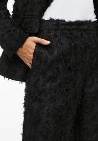 Black textured suit featuring frayed detailing; includes a pocket on the pants and a slightly oversized blazer. Material appears soft and layered.