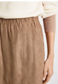 Ruskea mokkanahkahame, jossa on kerätty joustovyötärö. Sileä pinta, jossa on pystysaumat. Pehmeä, vaimea väri sopii erilaisten asujen kanssa.