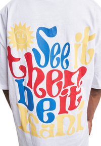 White cotton t-shirt featuring bold, multicolored text in red, blue, yellow, with curved letters and a yellow sun graphic on the upper left.