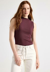 Bordeaux ribbetærkær uden ærmer med en bølgekant, parret med lysebeige højtaljede jeans. Glat tekstur og tætsiddende design.
