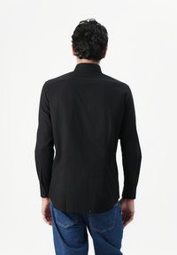 Svart langermet skjorte med rett bakdesign, knappede mansjetter og glatt tekstur. Kombinert med blå denimbukser.