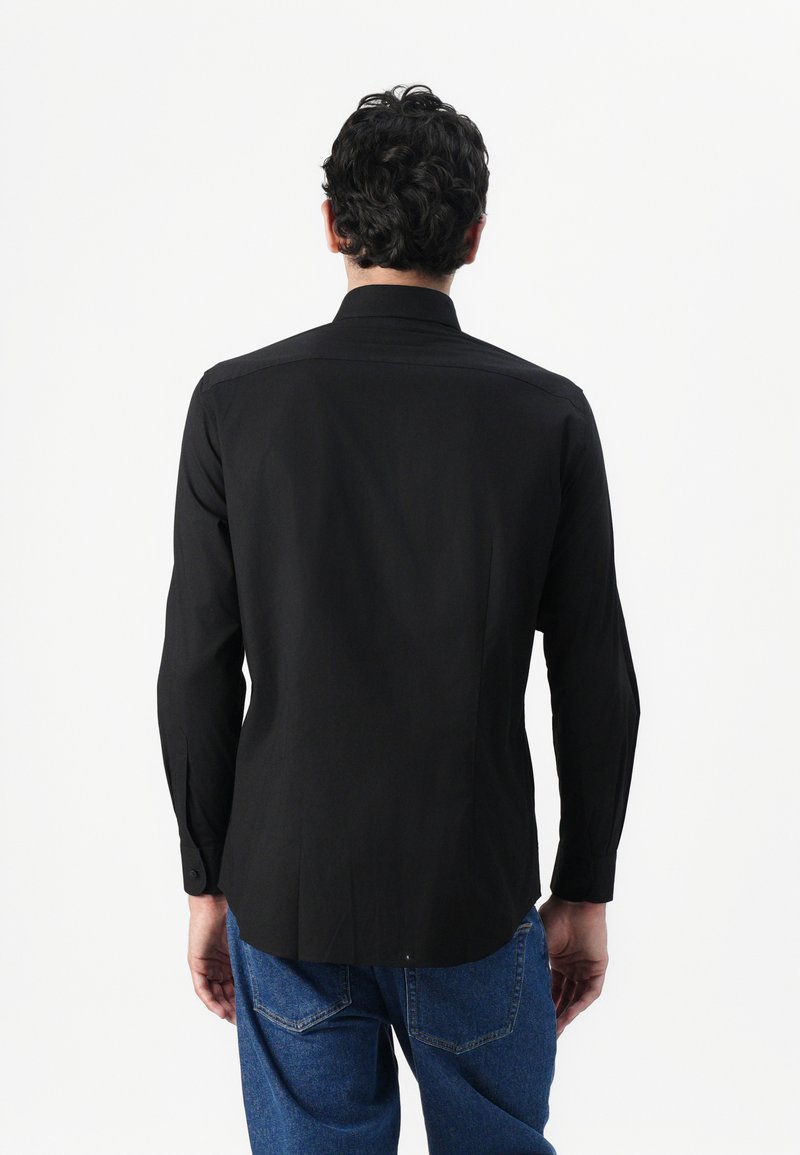 Black long-sleeve shirt featuring a straight back design, buttoned cuffs, and smooth texture. Paired with blue denim trousers.