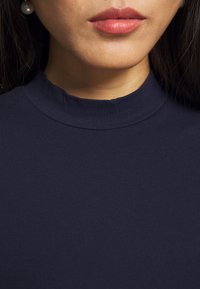 Granatowa bluzka o wysokim kołnierzu wykonana z prążkowanej tkaniny, cechująca się gładką fakturą i dopasowanym krojem, prezentująca czysty dekolt.