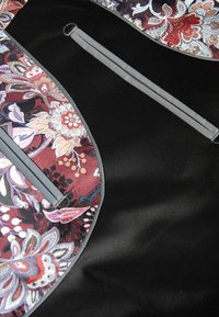 Bloemmotief stof in tinten van rood, paars en wit, omrand door zwart gestructureerd materiaal met twee grijze accentritsen.