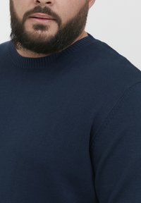 Suéter de cuello redondo azul marino hecho de un material de punto texturizado, con puños y cuello de canalé y sutiles detalles de costura en los hombros.