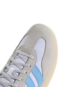 Grå mockaskor med vita tygpaneler och ljusblå detaljer. Har platta grå snörningar och en texturerad gummisula.