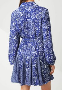 Blau gemustertes Kleid mit langen Ärmeln, das eine Mischung aus floralen und geometrischen Designs zeigt, mit tailliertem Bund und plissiertem Rock.
