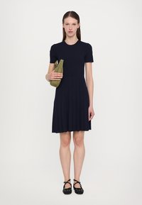 Navy ribbed dress with a fitted bodice and flared skirt. Styled with a green clutch and black flat shoes featuring a dotted design.