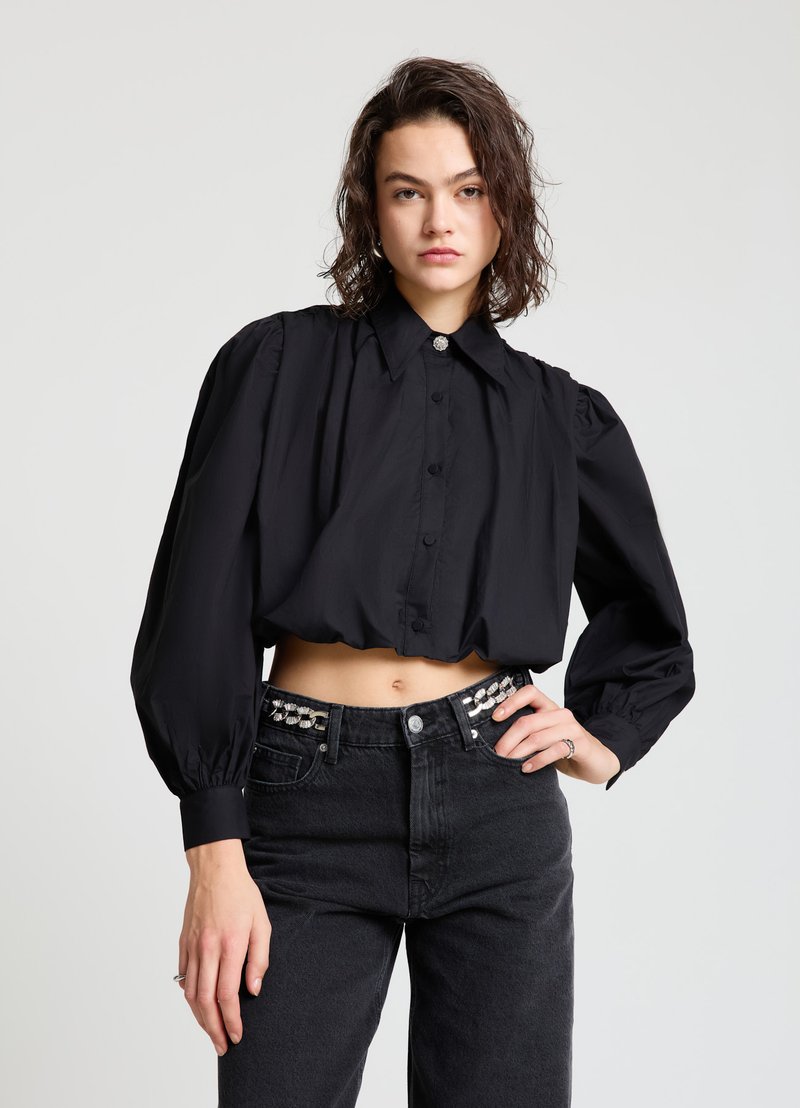 Schwarze, kurz geschnittene Bluse mit Knopfleiste, hohem Kragen und gepufften Ärmeln. Kombiniert mit hoch taillierten schwarzen Jeans mit dekorativen silbernen Gürtelakzenten.