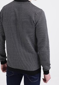 Svart och vit mönstrad tröja med ribbad krage och nederkant, med en stickad textur och figurnära design. Ryggvy visas.