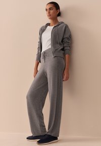 Gray knit hoodie with a zipper and drawstring waist paired with matching wide-leg pants. Model wears navy sneakers. Smooth texture.