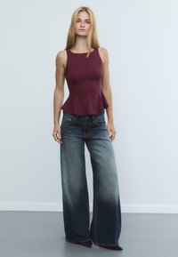 Top peplum bordeaux con un corsetto aderente; abbinato a jeans in denim blu sbiadito a gamba larga con un effetto gradiente di colore. Texture complessiva liscia.