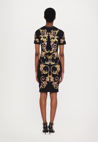 Rochie ajustată neagră cu modele florale colorate și volute. Mâneci scurte și tiv până la genunchi. Pur și simplu cu pantofi cu toc înalt negri.