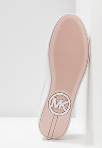 Semelle de chaussure avec une base en caoutchouc texturée rose clair, présentant un cercle de logo blanc avec "MK", et un accent blanc lisse le long du bord.