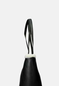 Borsa nera in pelle con due manici lunghi, caratterizzata da un morbido bordo di pelliccia bianca sulla parte superiore. Texture liscia con una forma conica.