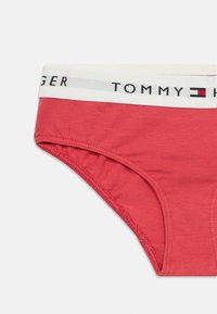 Crvene pamučne gaće s mekom teksturom, s bijelim pojasom na kojem piše "TOMMY HILFIGER" u crnom i crvenom slovima.