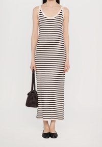 Robe maxi en tricot rayée noir et blanc avec un décolleté en scoop, texture côtelée et silhouette ajustée. Portée avec un sac sombre texturé et des ballerines noires.