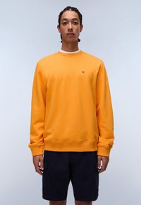 Orange crewneck sweatshirt med ribbede manchetter og kant, med et lille flerfarvet logo på brystet. Sammen med navy shorts.
