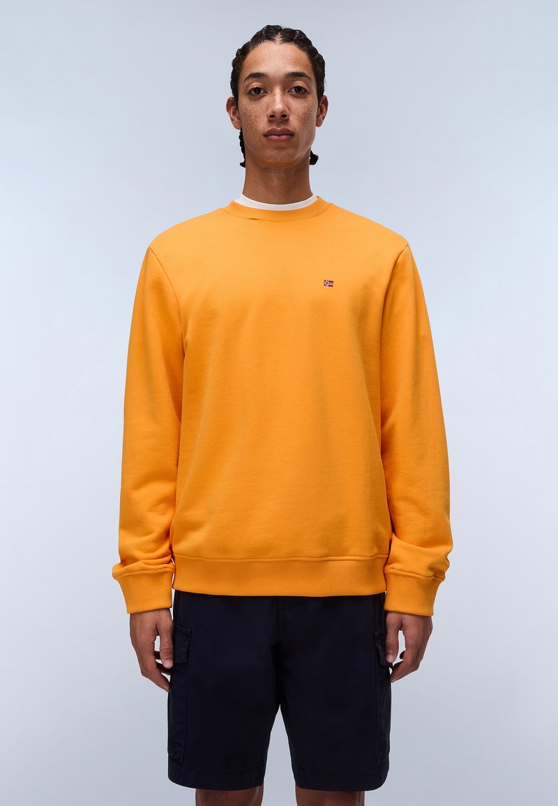 Orange crewneck sweatshirt med ribbede manchetter og kant, med et lille flerfarvet logo på brystet. Sammen med navy shorts.