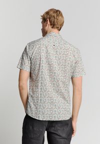 Kurzarmhemd mit geometrischem Muster in Pastellfarben. Aus leichtem Stoff gefertigt, mit Knopf am Rückenkoller und lockerer Passform.
