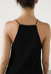 Mustassa ribattu toppi, jossa on kapeat olkaimet ja korkea kaula-aukko takana. Tekstuuri on sileä ja istuva.