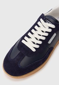 Marineblå sneakers lavet af læder og ruskind, med hvide snørebånd, en gummisål og kontrastfarvet syninger.