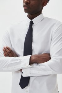 Witte lange mouwen overhemd met knoopmanchetten en een klassieke kraag, met een donkerblauwe stropdas. Glad stof met minimale textuur.