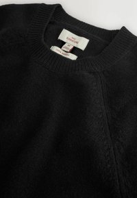 Schwarzer Merinowolle-Pullover mit Rundhalsausschnitt. Verfügt über gerippte Bündchen und Saum sowie gewebte Etiketten mit Größen- und Materialinformationen.