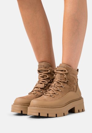 Tan farvet vandrestøvler med en tekstureret overdel i ruskind og syntetisk materiale, der har en polstret krave, runde snørebånd og tykke, robuste såler i gummi.