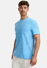 Hellblaues T-Shirt aus weichem Stoff mit Rundhalsausschnitt, kurzen Ärmeln und einer Brusttasche. Es hat ein strukturiertes Oberteil und einen glatten unteren Bereich.