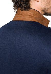 Granatowy sweter z fakturowanym brązowym kołnierzem z filcu. Projekt charakteryzuje się gładką, dopasowaną sylwetką i widocznym szyciem wzdłuż kołnierza.