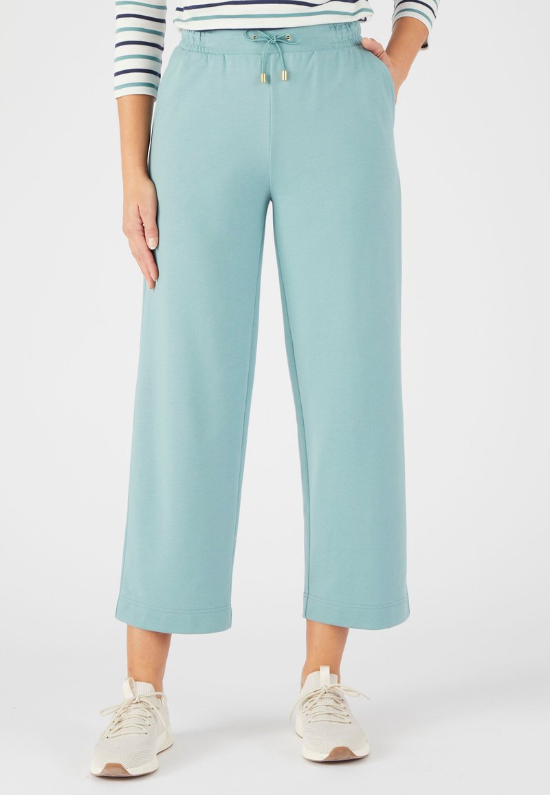 Lichtblauwe, cropped loungebroek met een elastische tailleband en trekkoorddetails, gemaakt van zachte stof, gecombineerd met crèmekleurige sneakers.