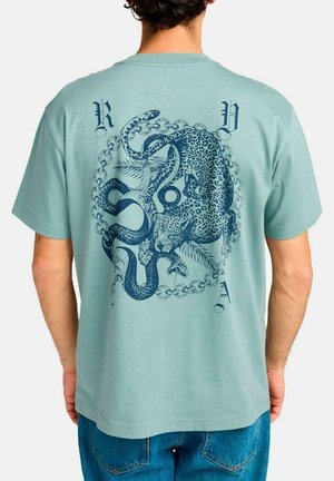 Camiseta de manga corta en un suave tono verde azulado, con un gráfico azul de un leopard y una serpiente dentro de un patrón de cadenas en la parte posterior.
