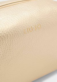 Pochette cosmetica color oro realizzata in materiale sintetico texturizzato. Caratterizzata dal logo "LIU JO" impresso e da una chiusura con cerniera liscia.