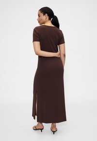 Brązowa sukienka maxi z krótkimi rękawami, z bocznym rozcięciem i miękką, gładką tkaniną. Widok od tyłu ukazuje luźny fason i prosty dekolt.